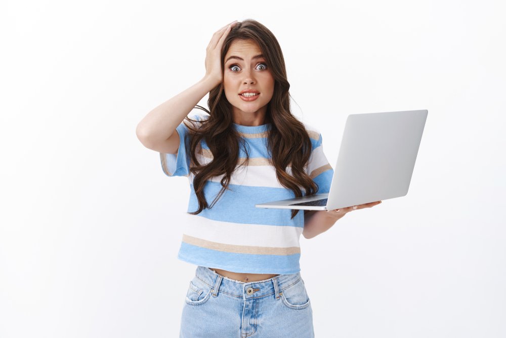 Oops my fault. Clumsy cute and silly woman brunette with curly long haircut, hold laptop, say yikes stare camera grab head, making mistake, have slight accident, apologizing white background